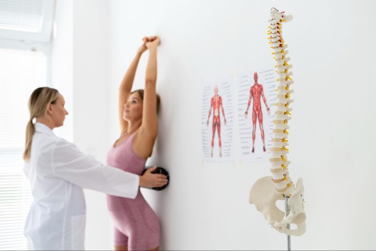 escoliose-adolescentes-observacao-postural Profissional de saúde a observar o alinhamento postural de uma adolescente durante uma consulta. Caption: A observação postural pode fazer parte da avaliação clínica quando existe suspeita de escoliose.